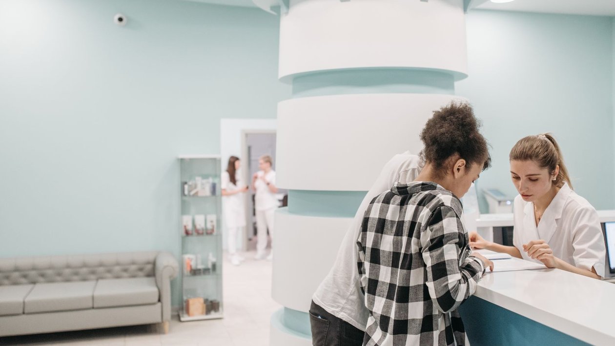 Patients review paperwork with a staff member at a bright medical clinic reception desk.