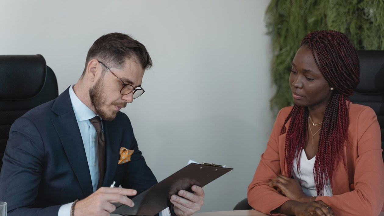 Hiring manager reviewing a clipboard while interviewing a candidate at an office table.