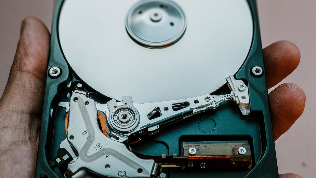 A hand holds an opened hard drive, showing the shiny disk platter and the read arm inside.