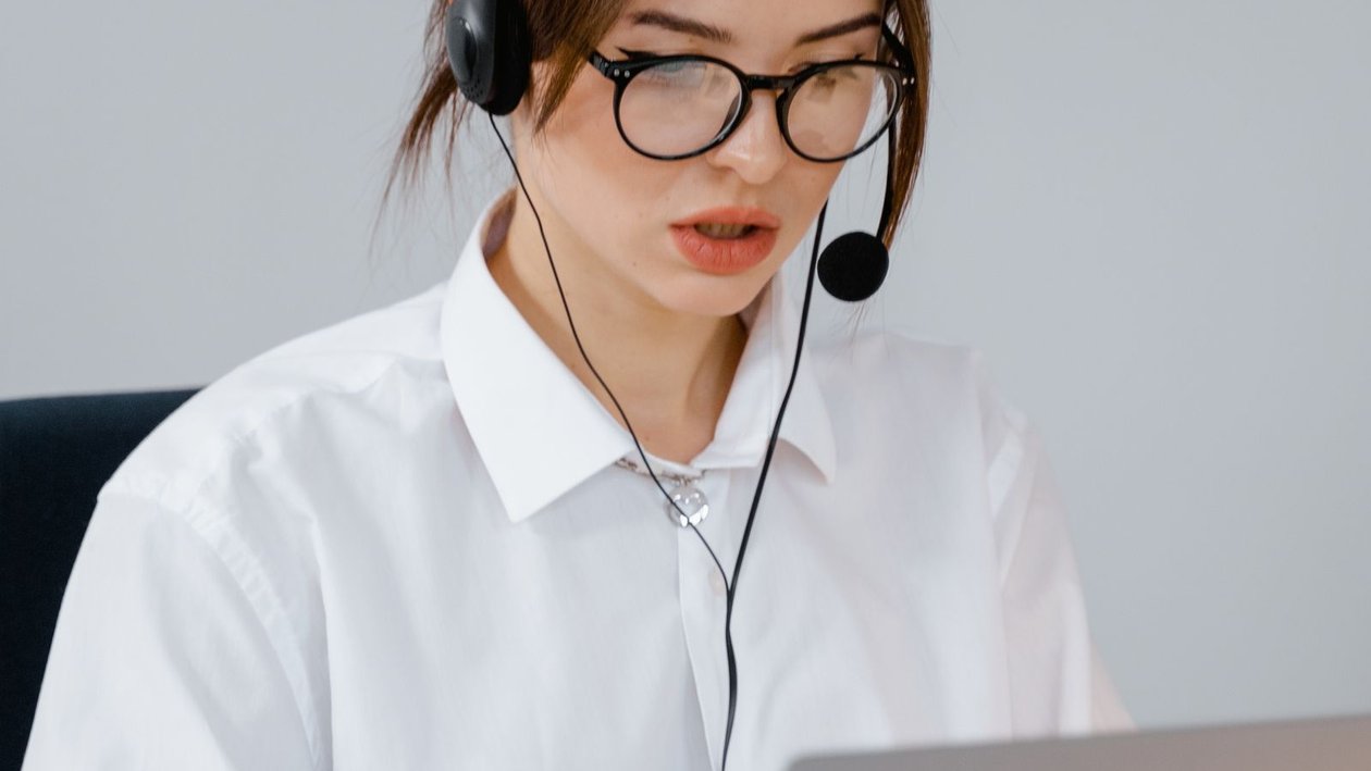 A customer support agent wearing a headset speaks with a caller while working at a laptop.